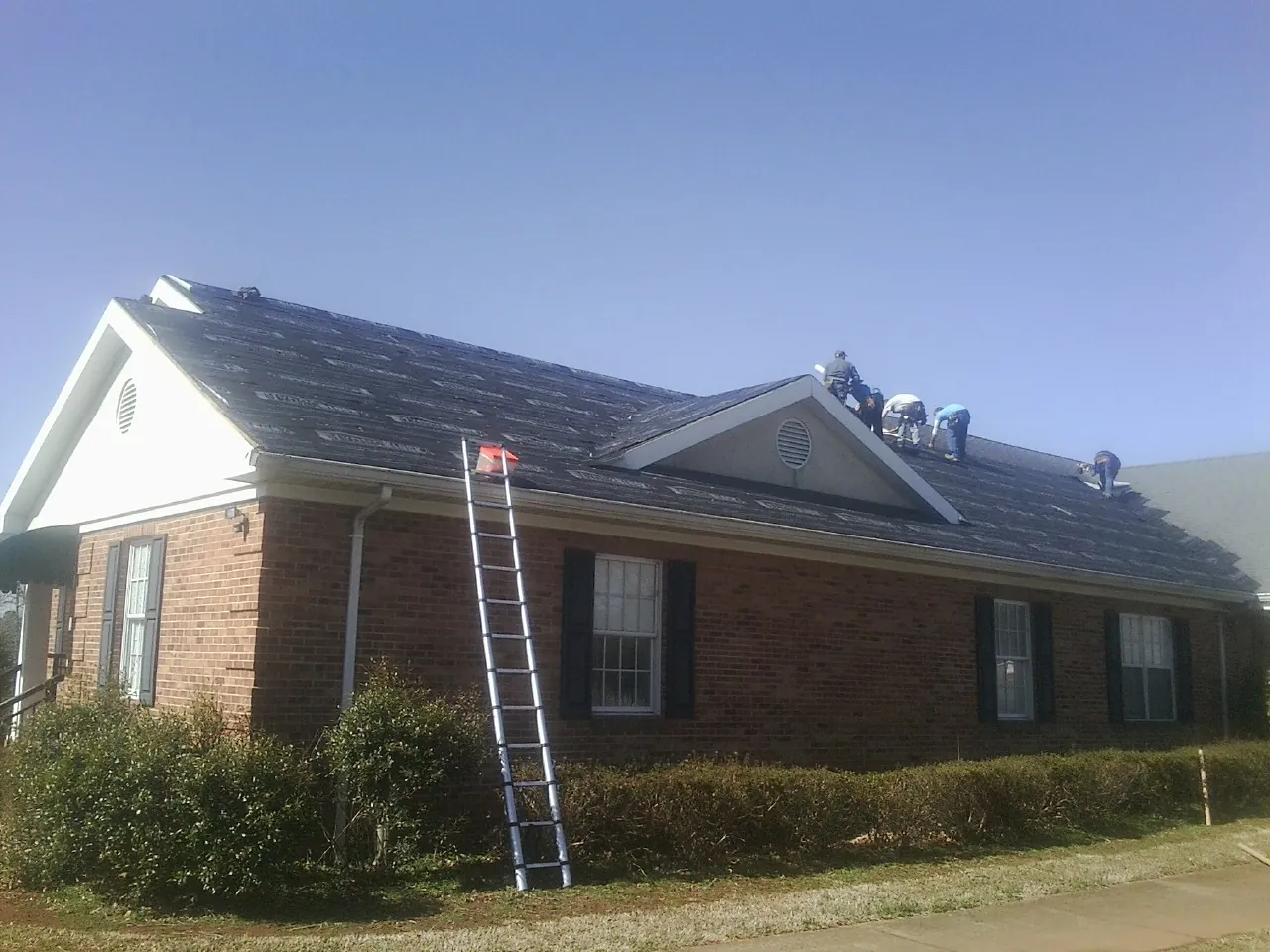 Crew tearing shingles off a brick ranch roof with a ladder set — Emergency Roof Repair work by our crew in Highland Mills