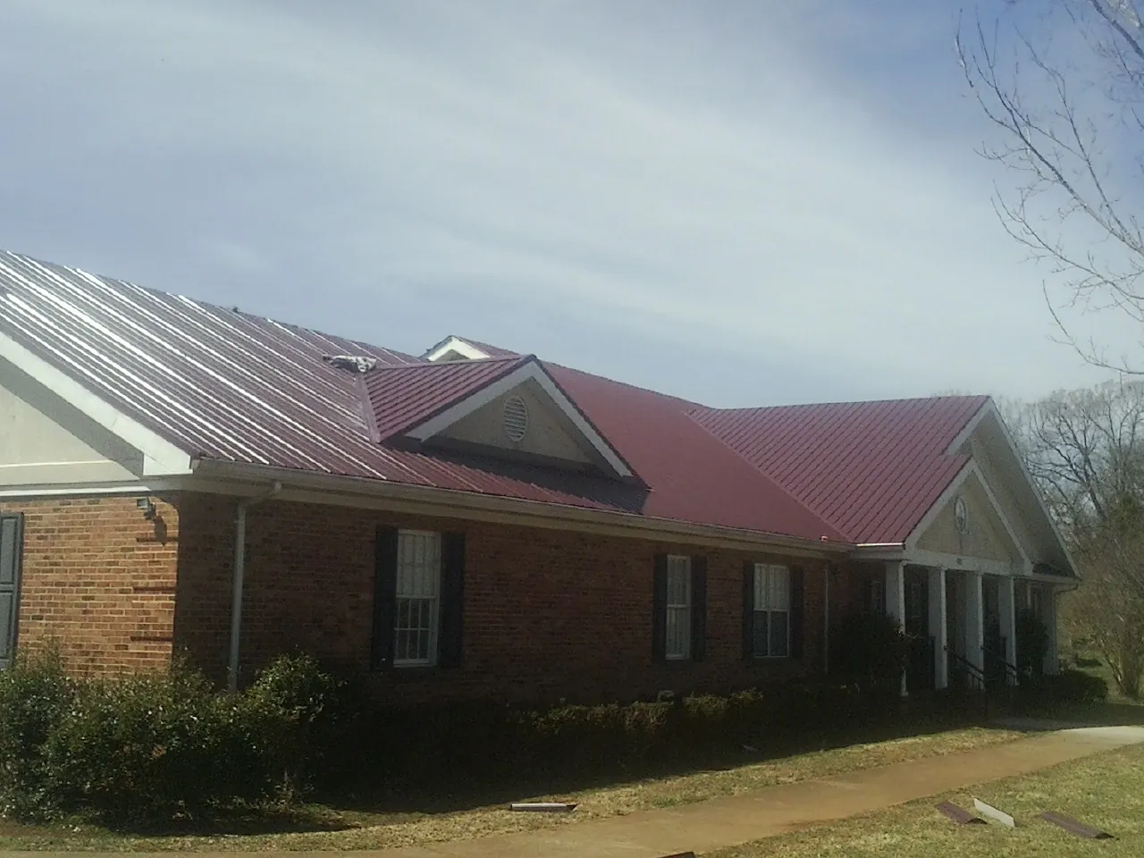 Red metal roof with gabled entries on a long brick building, from a Hail Damage Roof Repair job in Highland Mills