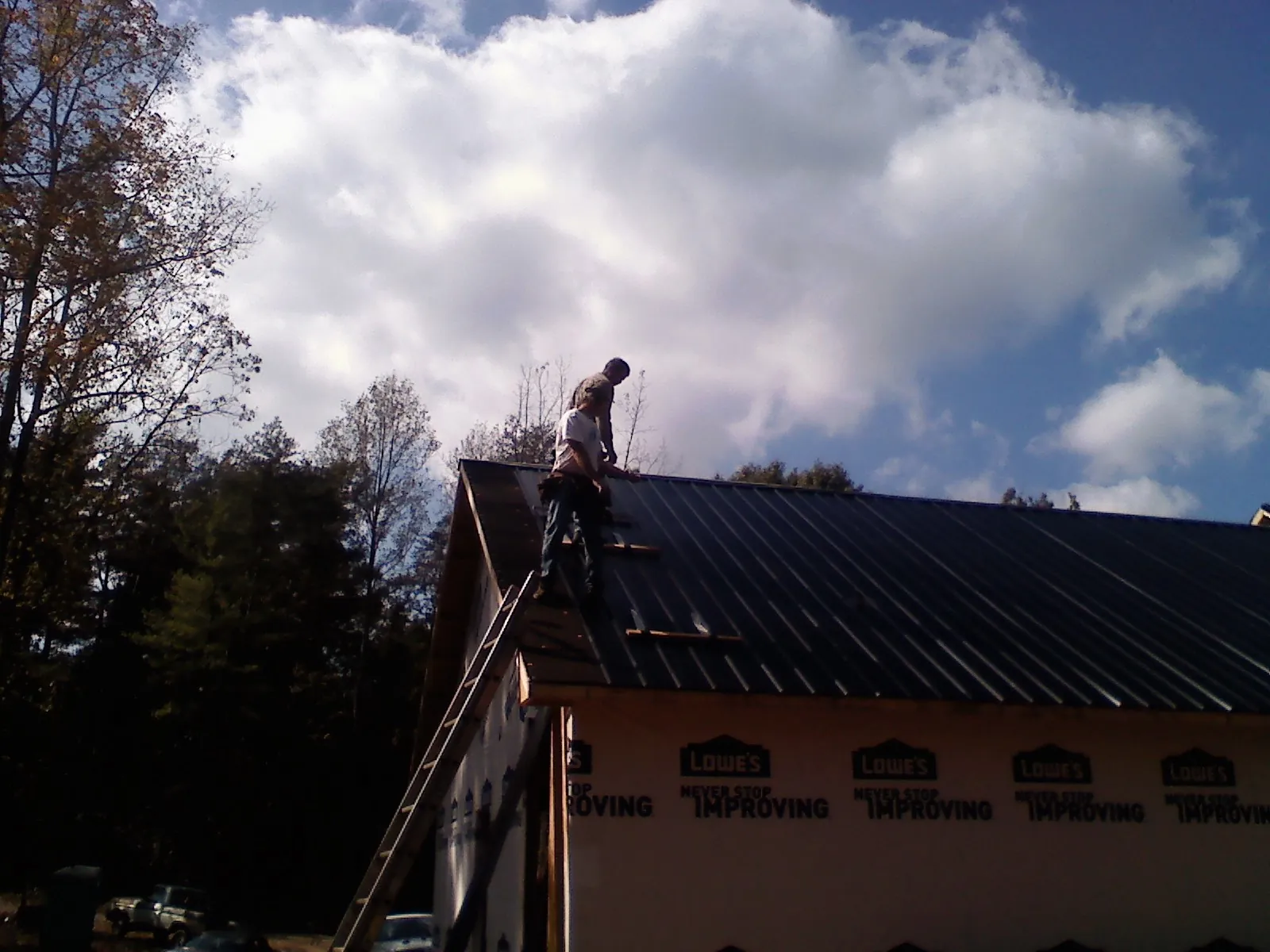 Roofer fastening dark metal panels high against a cloudy sky, from a Roof Inspection job in Highland Mills