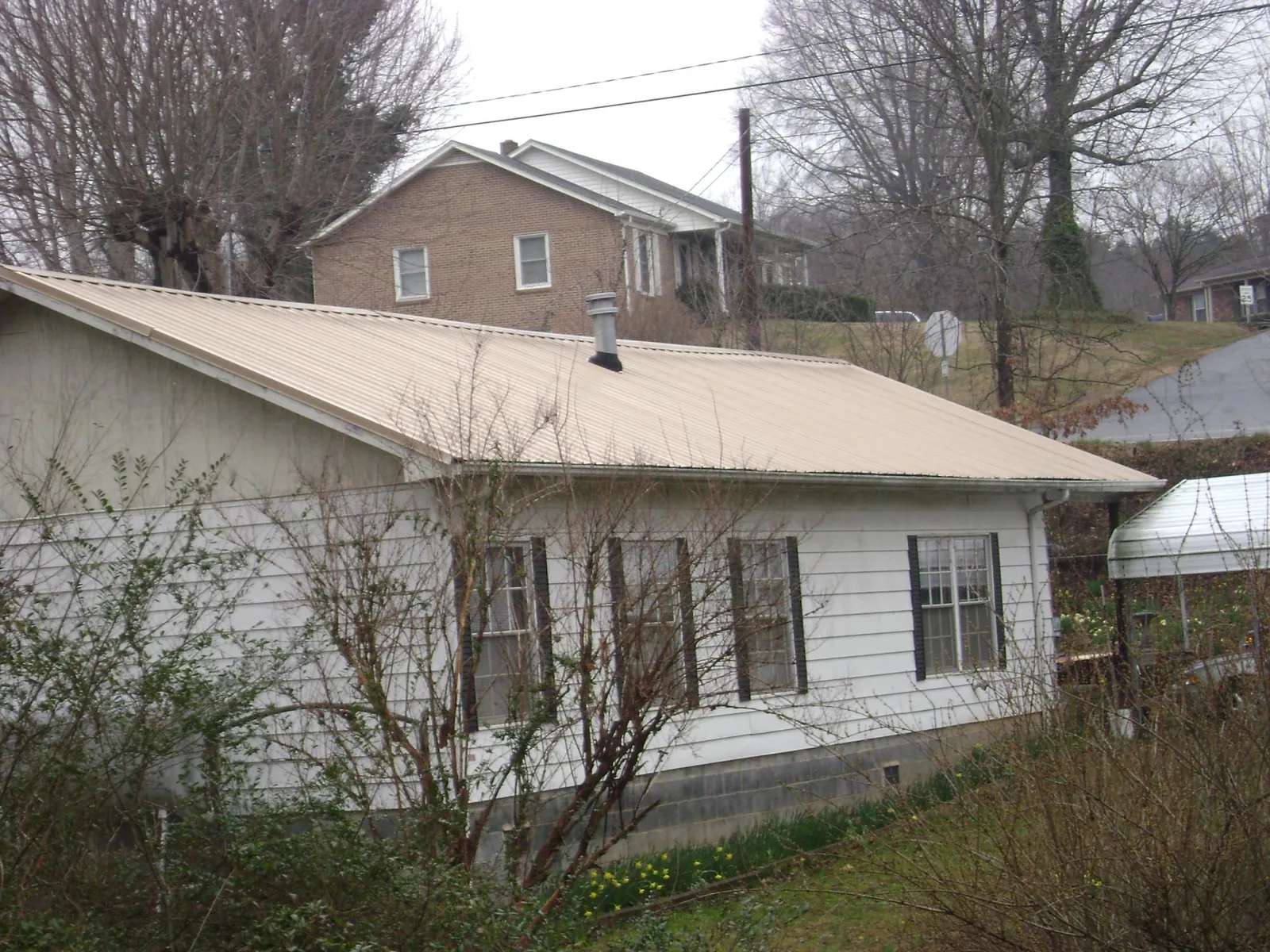 Tan metal roof on a white sided house set into a hillside — Commercial Roofing by Roofing Brothers in Highland Mills